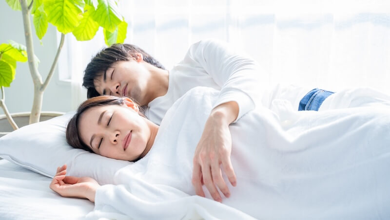 ベッドで眠る若い夫婦